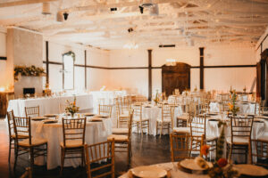 Live Oak Venue space with white tablecloths draped on round tables and gold chiavari chairs.