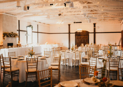 Live Oak Venue space with white tablecloths draped on round tables and gold chiavari chairs.